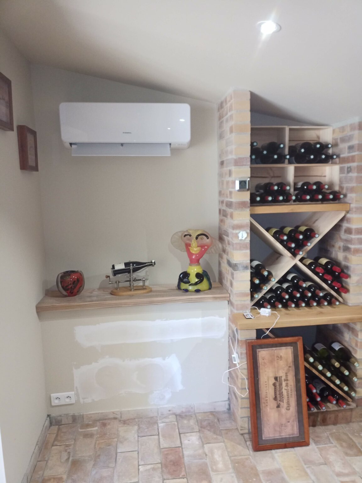 Unité intérieure murale de climatisation réversible posée en hauteur au-dessus d'un casier à vin, pièce en pierre et tomettes — MSC Climatisation, Var