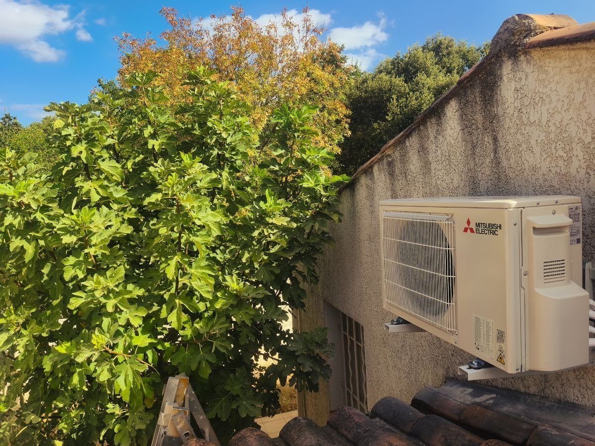 Le groupe extérieur, fixé sur deux équerres murales, vu de côté. Groupe extérieur Mitsubishi Electric d'une climatisation réversible bi-split, fixé sur équerres murales au-dessus d'un toit de tuiles, maison à Sainte-Maxime