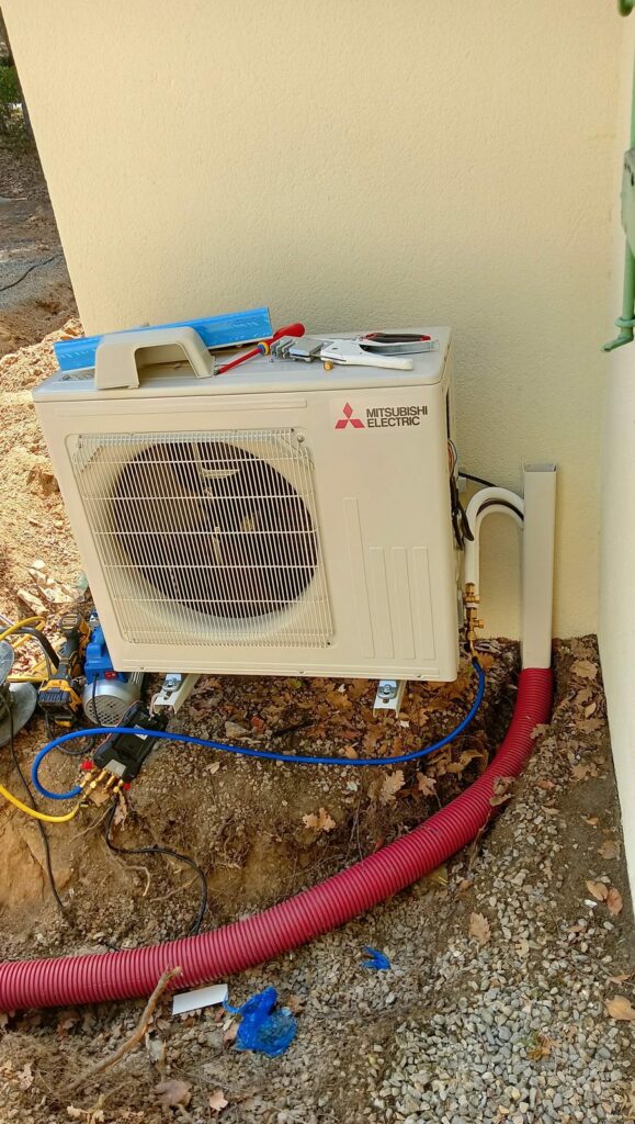 Groupe extérieur Mitsubishi Electric au pied du mur, liaisons sortant de leur gaine enterrée vers la goulotte, pompe à vide et manomètre branchés – MSC Climatisation