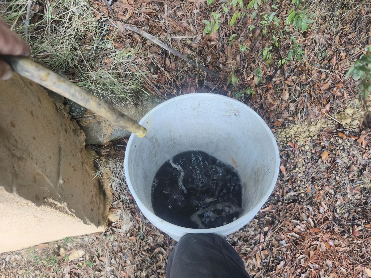 Seau d'eau noire chargée de boues sortie du circuit de chauffage au début du désembouage
