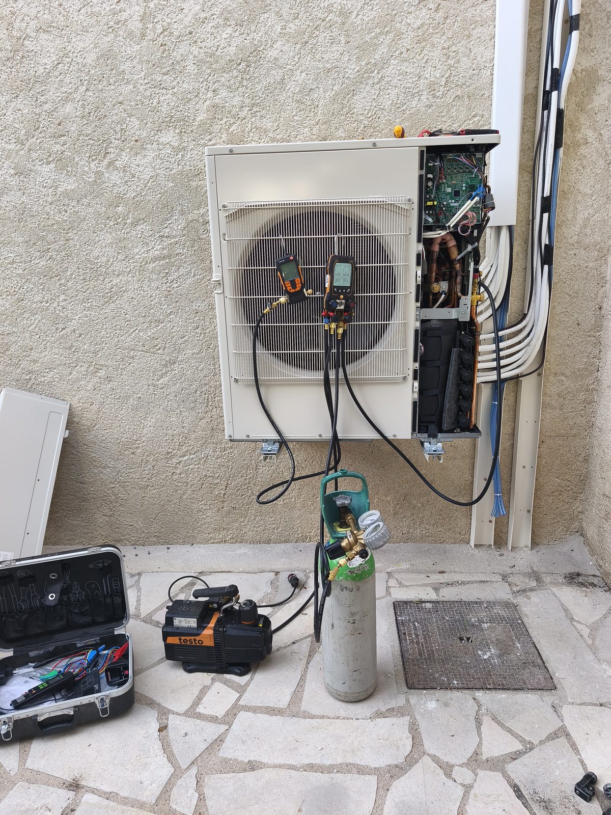 Groupe extérieur ouvert fixé sur équerre murale, deux manomètres électroniques accrochés, pompe à vide, bouteille d'azote et valise d'outils sur la terrasse — MSC Climatisation
