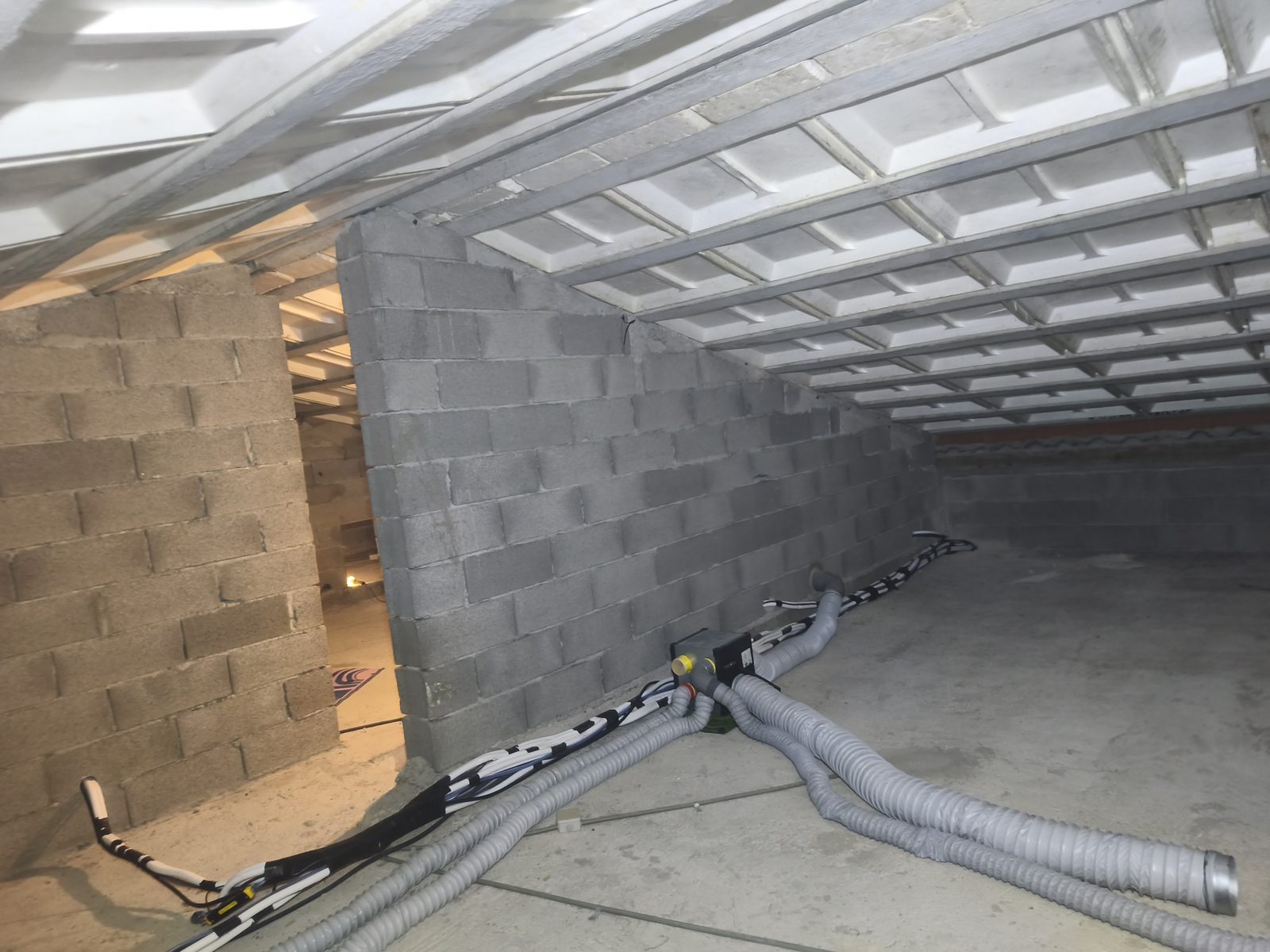 Combles sous toiture, faisceau de liaisons frigorifiques gainé posé le long d'un mur en parpaings, gaines grises de ventilation à côté — MSC Climatisation