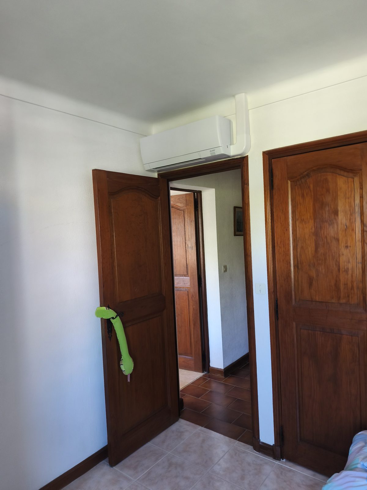 Chambre aux murs blancs, unité murale blanche posée au-dessus de la porte en bois — MSC Climatisation