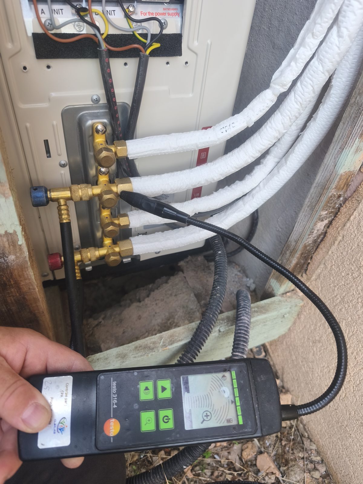 Détecteur de fuites électronique tenu en main, sa sonde sur les raccords frigorifiques d'un groupe extérieur multi-split — MSC Climatisation