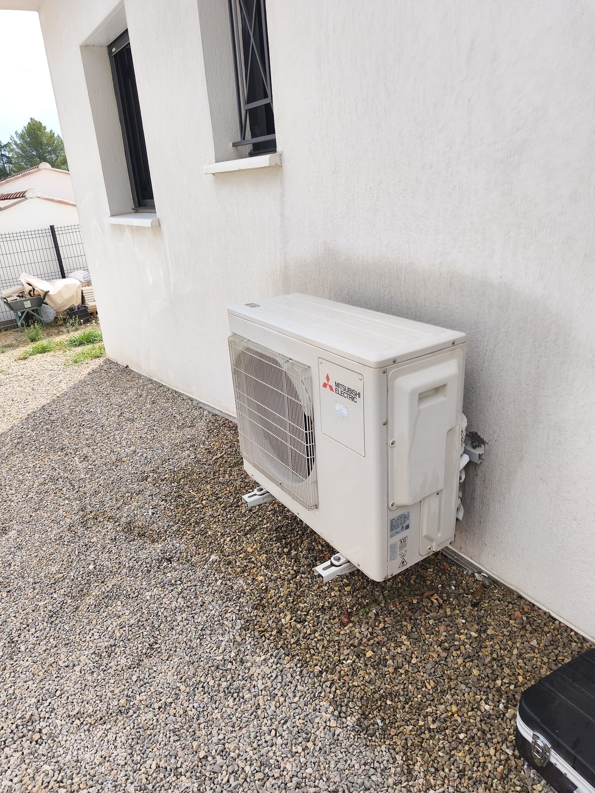 Groupe extérieur de climatisation Mitsubishi Electric fixé sur pattes le long d'un mur de maison — MSC Climatisation