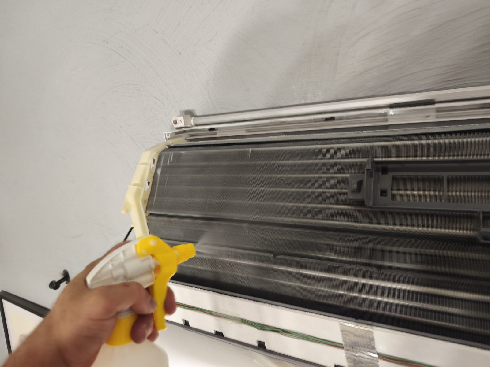 Pulvérisateur manuel dirigé sur la batterie d'une unité murale de climatisation démontée — MSC Climatisation